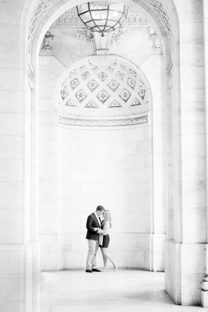 engaged couple standing inside the marble façade of the NY Public Library