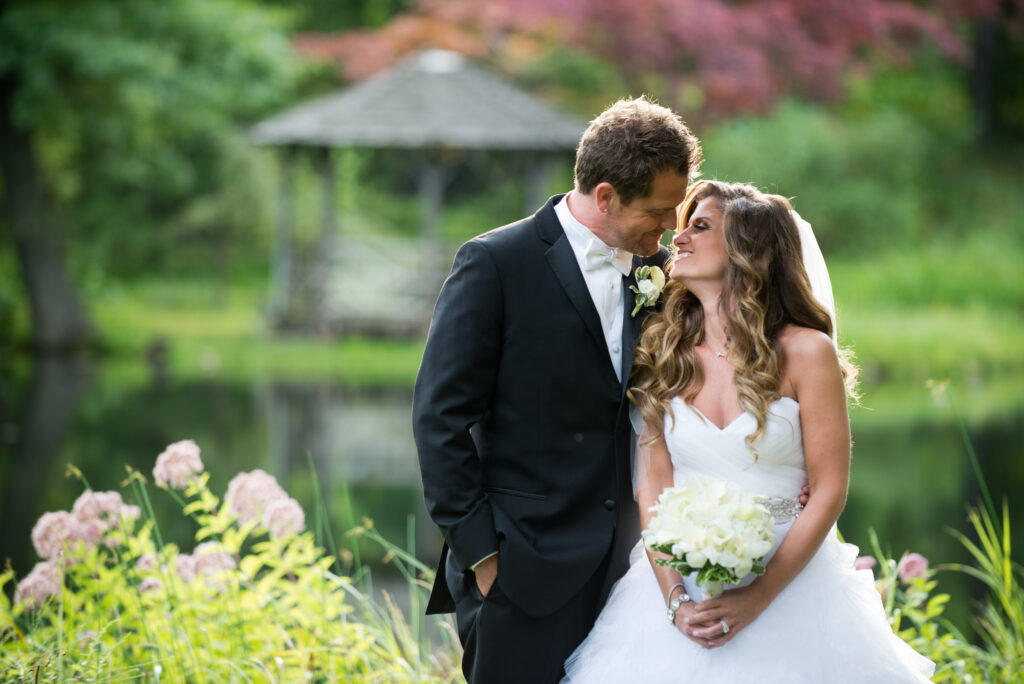 half length photo of a bride and groom just about to kiss outside overlooking a pond