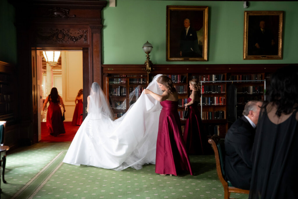 bride getting ready to leave her getting ready room for the ceremony with her bridesmaids holding the train of her dress
