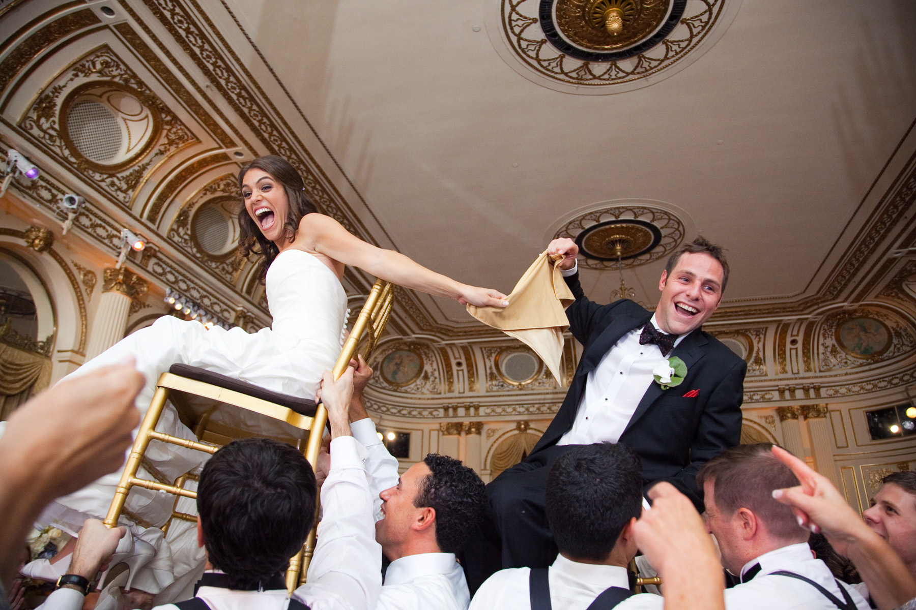 Bride and groom during the hora up in chairs at The Plaza Hotel, New York City